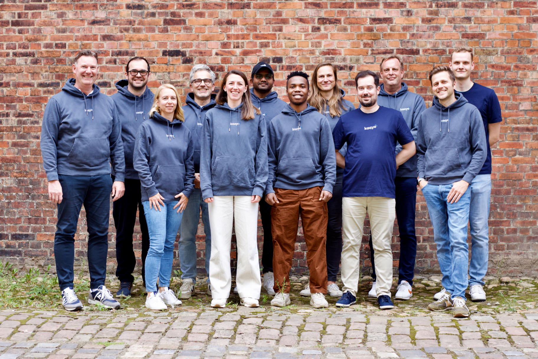 kaayo Teammitglieder in Marken-Hoodies stehen zusammen vor einer Backsteinwand